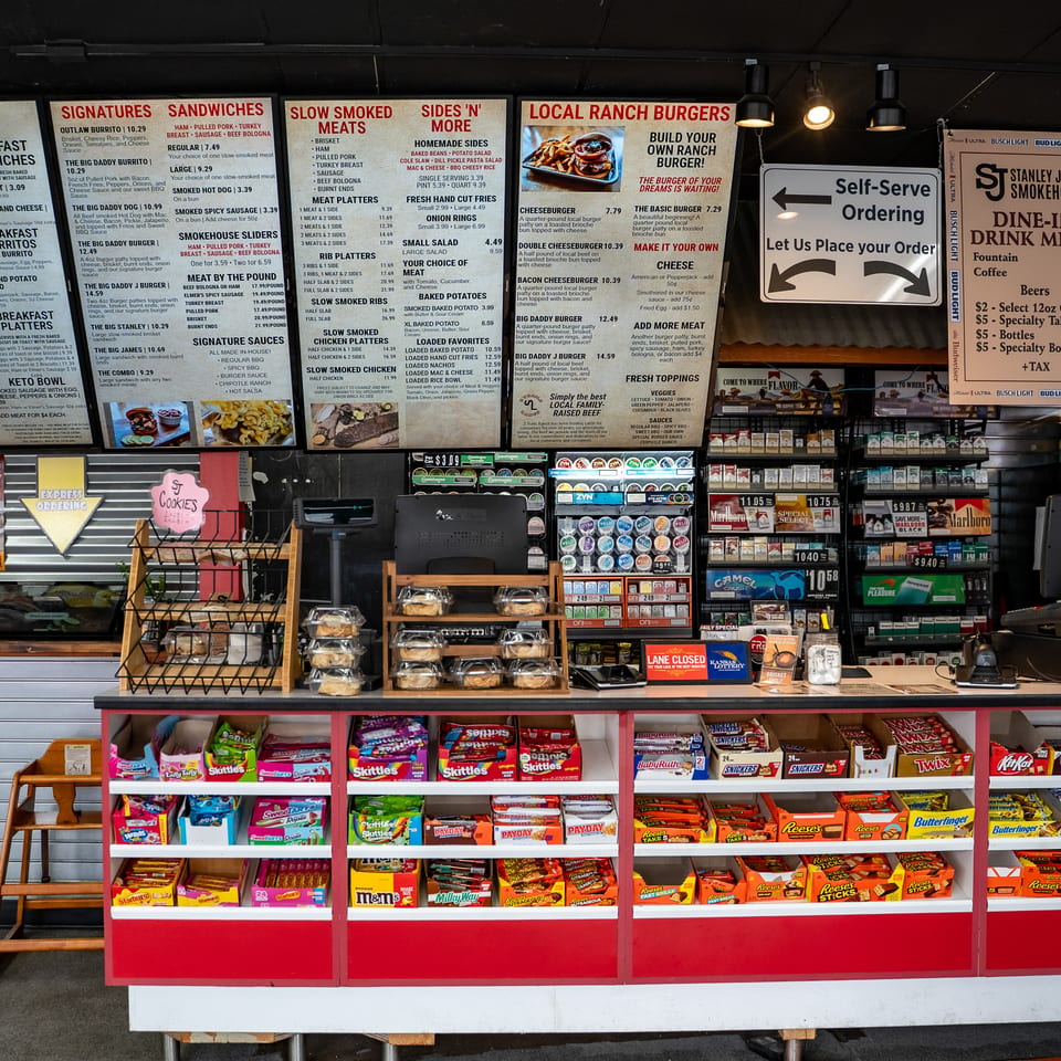 Stanley James Smokehouse counter displays breakfast, barbecue, burgers, self-service ordering, snacks, candy, and tobacco products.