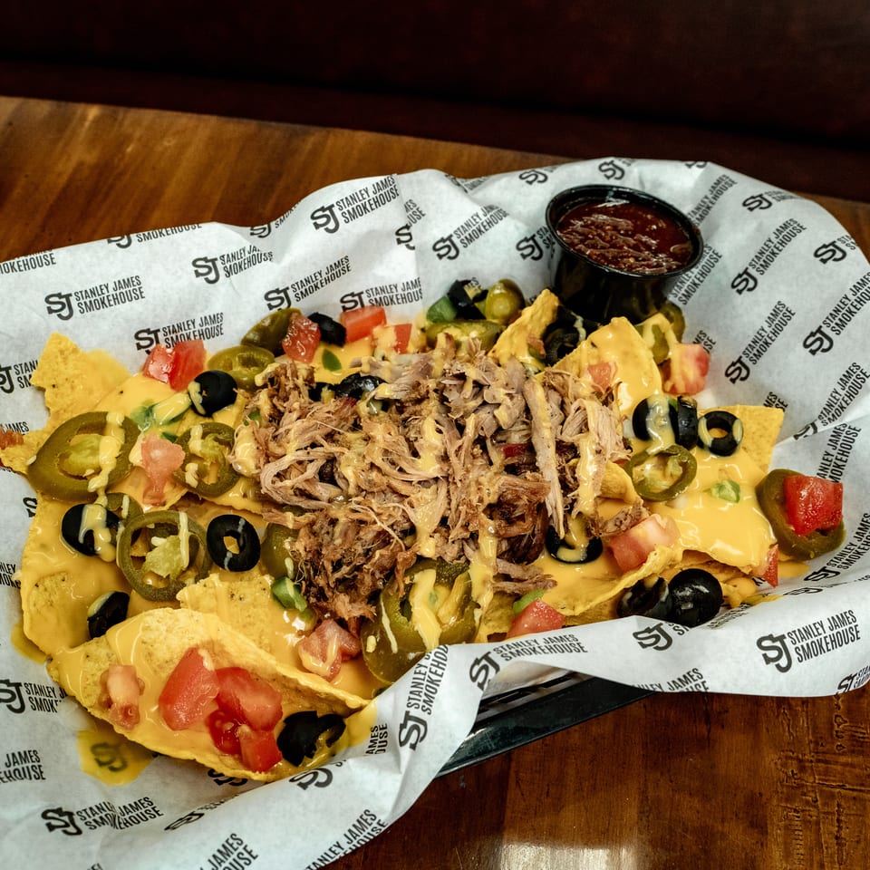 Loaded nachos topped with pulled pork, cheese sauce, jalapeños, tomatoes, olives, and salsa at Stanley James Smokehouse.