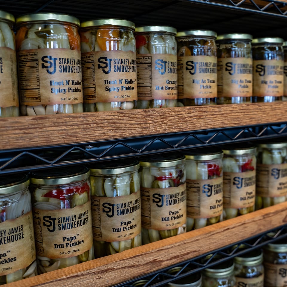 Shelves stocked with jars of Stanley James Smokehouse dill and spicy pickles.