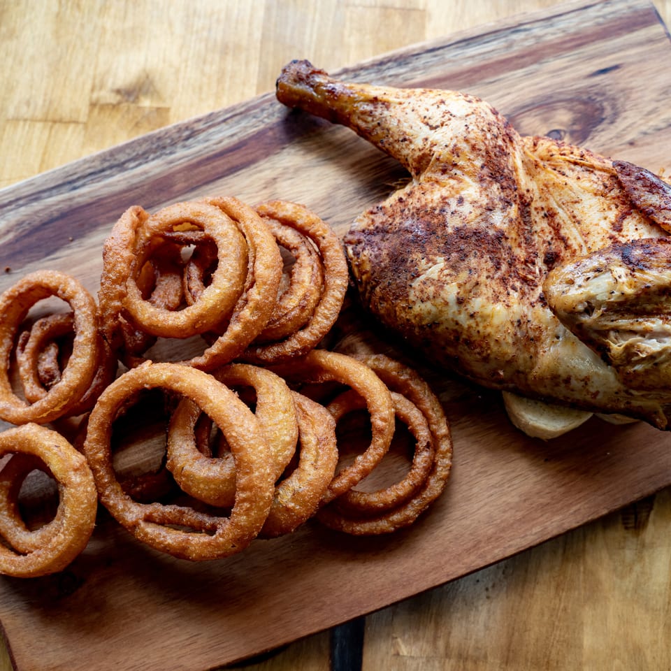 Seasoned roasted chicken served with crispy onion rings on a rustic wooden serving board.