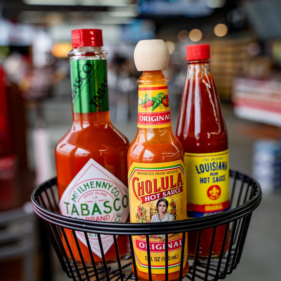 Basket of assorted hot sauces, including Tabasco, Cholula, and Louisiana brands, on a restaurant table.