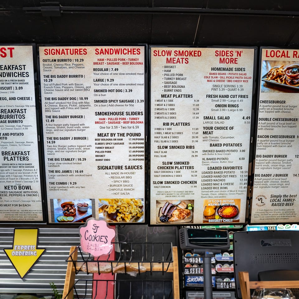 Restaurant menu boards display breakfast, sandwiches, smoked meats, sides, and customizable local ranch burgers at Stanley James Smokehouse.